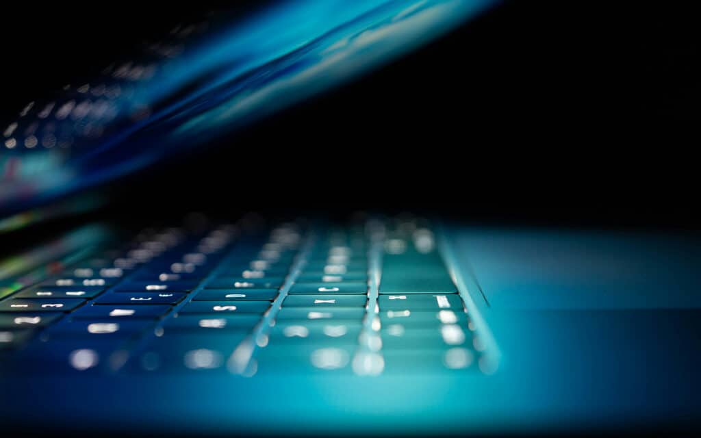 Image of computer laptop being opened with blue light from screen illuminating keyboard